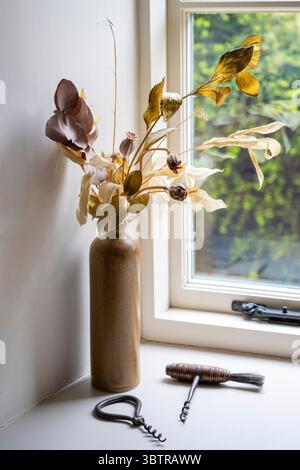 Dried flowers with seed heads and a display of corkscrews by a cottage window in England Stock Photo