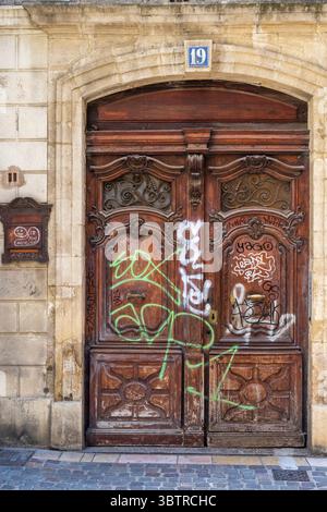 Graffiti daubed on an ancient traditional front door despoiling its elegance in Avignon, Vaucluse department, South East France Stock Photo