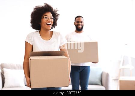 Excited African Couple Carrying Moving Boxes Entering Own Home Stock Photo