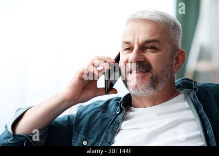Happy mature man having conversation on smartphone at home Stock Photo