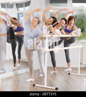 Elderly woman stretching at barre with group of adult ballet beginners Stock Photo