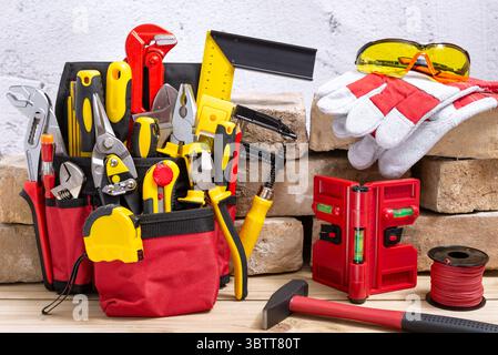 Belt bag with various hand tools leaning on an old bricks on a wooden table. Selective focus. Stock Photo