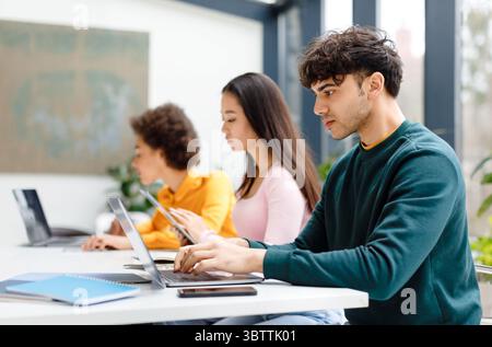 Multiracial male and female students studying for test, making homework with gadgets, focused guy using laptop Stock Photo