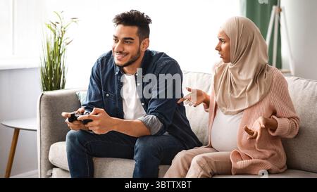 Pregnant muslim lady offended to her careless husband playing video games Stock Photo