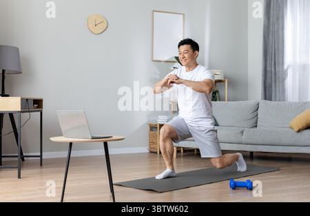 Motivated asian man exercising at home, using laptop Stock Photo