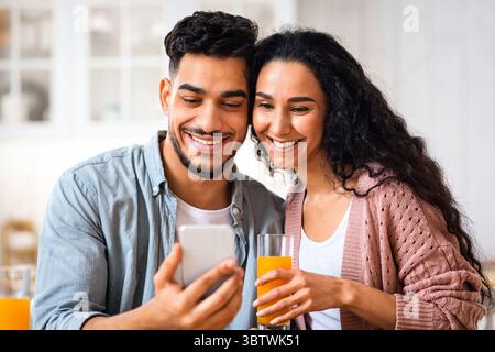 Portrait Of Happy Arab Couple Watching Videos On Smartphone And Having Breakfast Stock Photo