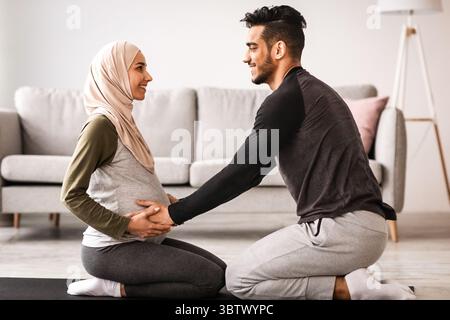 Pregnancy Workout. Happy Muslim Spouses Practicing Yoga Together At Home, Side View Stock Photo
