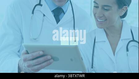 Reviewing tablet computer, two doctors in lab coats using stethoscopes analyzing data in exam room Stock Photo