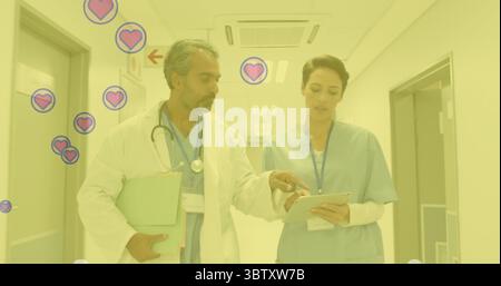 Walking doctor and nurse reviewing patient files in hospital corridor, using tablet and stethoscope Stock Photo