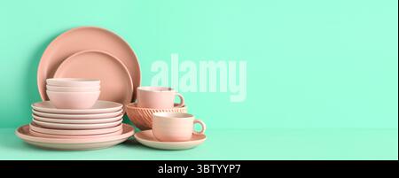Pink cups with plates and bowls on mint background with space for text Stock Photo