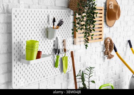 Pegboard with gardening tools on white brick wall in workshop Stock Photo