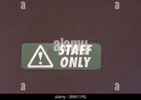 Close-up of a "STAFF ONLY" sign with a warning symbol on a dark textured surface. Green and white sign indicating restricted access. Stock Photo