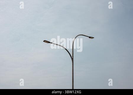 Minimalist view of a modern forked street light against a pale, cloudy sky. This image symbolizes urban infrastructure, simplicity, and modern design. Stock Photo