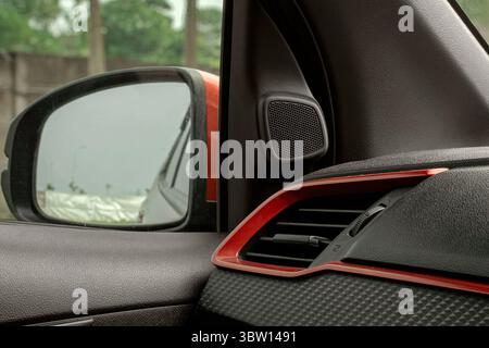 Close-up of a modern car interior, featuring the side mirror, tweeter speaker, and air vent with red accents and a carbon fiber texture. Stock Photo