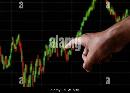 A human hand points towards a dynamic financial candlestick chart displayed on a dark background. Analysis, investment, and market trends concept. Stock Photo