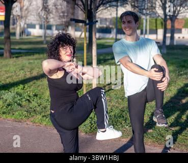 Personal trainer guiding mature woman doing leg exercise in park Stock Photo