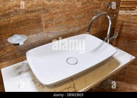 A modern ceramic sink with a sleek design sits on a marble vanity, paired with a chrome faucet, exuding elegance and functionality in a stylish bathro Stock Photo