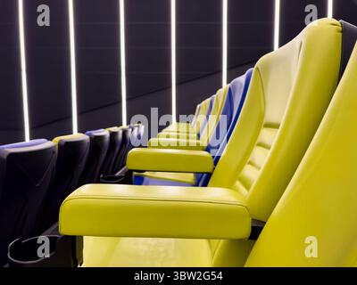 A row of yellow and blue chairs are lined up in a theater. The chairs are all facing the same direction Stock Photo
