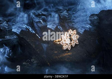 An elegant floral diamond-studded gold ring placed on dark charcoal with smoky, mystical vibes—highlighting brilliance and contrast. Stock Photo