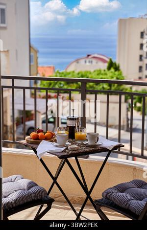 A cozy breakfast setting on a balcony overlooking the ocean, featuring orange juice, fruit, and coffee, creating a serene morning ambiance. Stock Photo