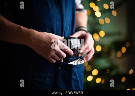 Waiter Takes The Wireless Pos Terminal From Pocket In A Restaurant At Christmas Stock Photo