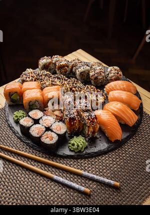 Assorted sushi arranged on a slate platter, showcasing a variety of rolls, nigiri, and wasabi, accompanied by chopsticks Stock Photo