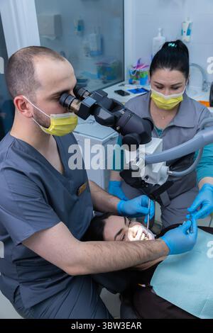 Dental professionals conduct a precise examination using a microscope while ensuring patient comfort and safety through proper protocols in a modern Stock Photo
