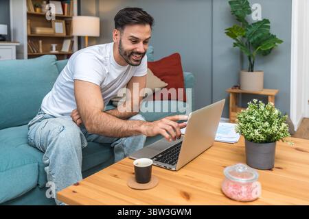 Young business man small startup company owner, working at home, checking the finances on graphs and laptop. Innovative young freelance male calculati Stock Photo