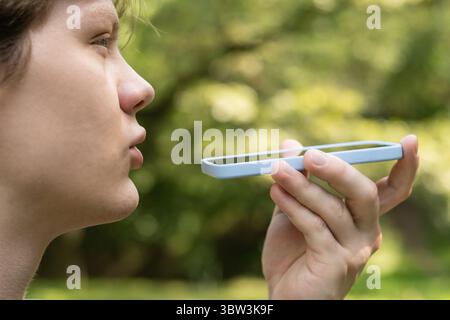 Young caucasian blond man recording voice message on cellphone. Man using virtual voice assistant. Outdoors. Close up Stock Photo