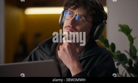 Thoughtful Hispanic guy thinking typing keyboard laptop at home programmer man working remote business freelancer searching information website Stock Photo