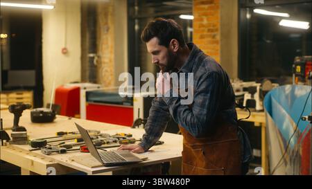 Cheerful Caucasian man wood master carpenter using laptop in workshop builder searching information in Internet guy male chatting social media network Stock Photo
