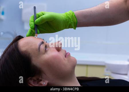 Professional Beauty Treatment Focused on Microblading Preparation with a Careful Artist Drawing Eyebrow Shape for Client in Modern Salon Space Stock Photo