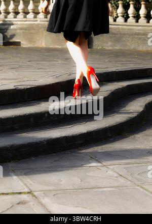 A person wearing red high heels walks up a set of stone steps. Stock Photo