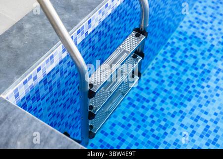 Close-up view of a blue-tiled swimming pool featuring a stainless steel ladder, representing relaxation, summer, and leisure activities in a modern de Stock Photo