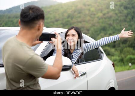 Joyful Adventure. Young woman enjoying a car ride while being photographed. Stock Photo