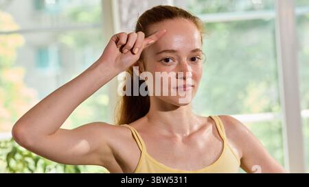 Portrait of sweaty focused woman in yellow top raising hand after workout session Stock Photo