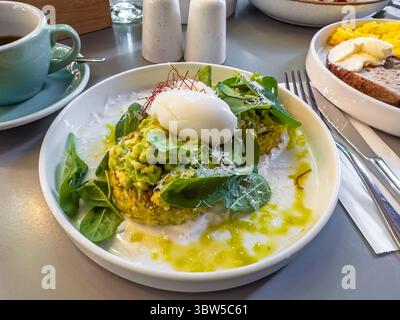 A delicious and healthy breakfast of zucchini fritters topped with smashed avocado, a perfectly poached egg, fresh spinach, and grated Parmesan cheese Stock Photo