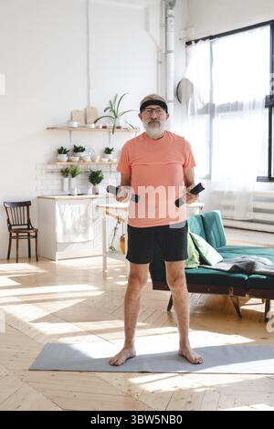 Senior man doing fitness exercise at home with dumbbells - elderly people and wellness health concept Stock Photo
