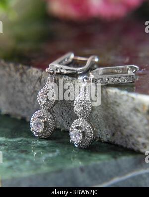 Pair of silver earrings with sparkling stones are laying on a green marble surface Stock Photo