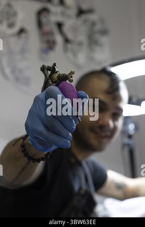 Tattoo artist out of focus smiling while showing the hand holding a tattoo machine in studio. Soria, Castilla y Leon, Spain Stock Photo