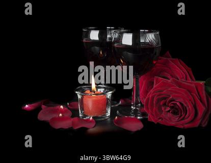 Valentine's Days concept: two glasses of red wine, two red roses and a burning red candle isolated on a black background Stock Photo
