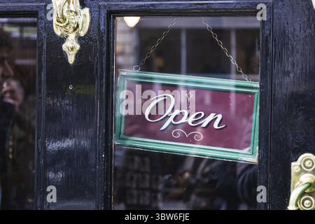 Bright open sign displayed in a window of a black painted storefront, indicating the business is welcoming visitors Stock Photo