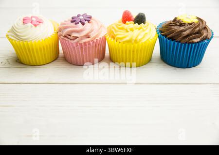 Four cupcakes are sitting on white tabletop in flat design with cream swirls and candy toppers Stock Photo