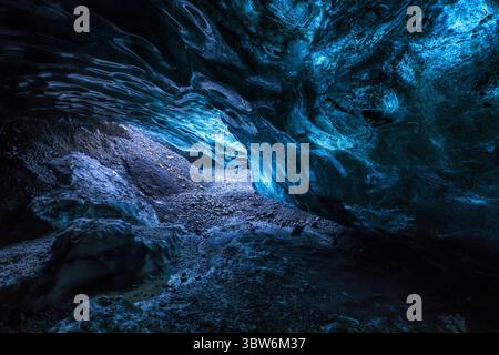 View of an ethereal ice cave, illuminated with vibrant blue light cascading over the rugged, textured ice formations, creating a mesmerizing spectacle, Iceland. Stock Photo