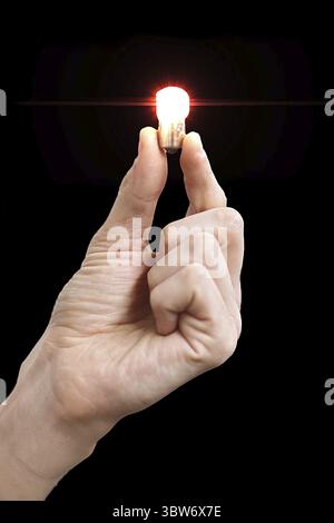 A man's hand holds a small glowing light bulb in his fingers. Isolate on a black background. Concept of an idea or inspiration. Blank for design Stock Photo