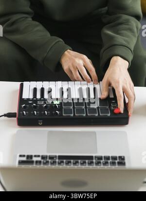 Man recording electronic music track with portable midi keyboard on laptop computer in home studio. Producing and mixing music beat making and arrangi Stock Photo