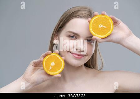 A woman is holding two oranges in her hands and smiling. Concept of happiness and positivity, as the woman is enjoying the simple pleasure of holding Stock Photo