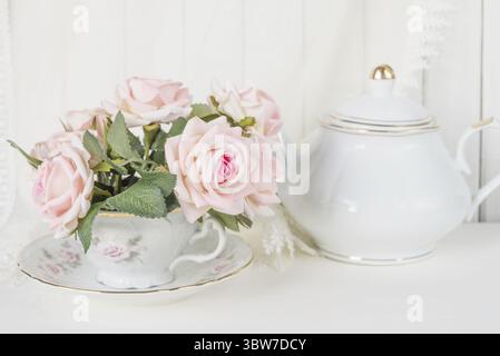 Beautiful still life: a graceful porcelain cup, white china teapot and pink rose flowers Stock Photo