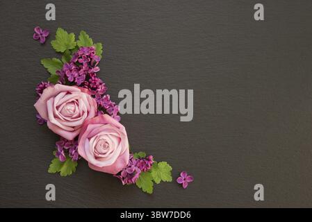 Decorative composition consisting of pink roses, violet lilac flowers and green leaves on a black slate. Flat lay, top view, overhead view Stock Photo