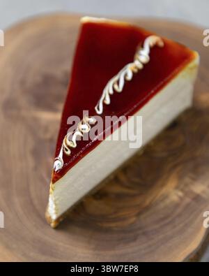 Slice of delicious cheesecake with red caramel topping sitting on wooden board Stock Photo